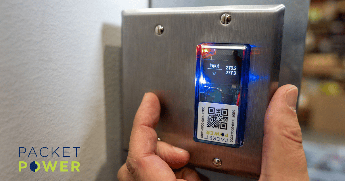 Small form factor wireless power monitor from Packet Power installed on a wall plate displaying real-time voltage readings for granular facility power monitoring